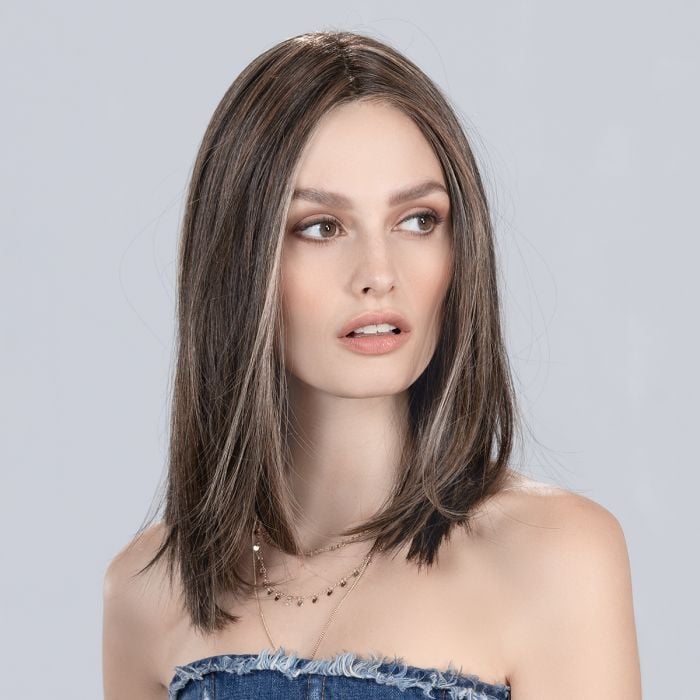 Model wearing a long straight brunette synthetic hair piece with highlights